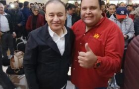 Dos asistentes posan durante un encuentro político en Hermosillo; uno viste una camisa roja con el emblema del PT