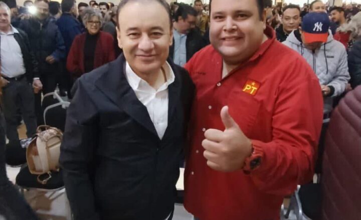 Dos asistentes posan durante un encuentro político en Hermosillo; uno viste una camisa roja con el emblema del PT
